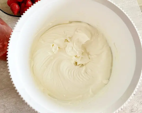 Gładki, puszysty **prosty krem z mascarpone bez śmietany** w białej misie, gotowy do deseru. Obok miski widać miseczkę z truskawkami.