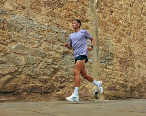 Uomo con tatuaggio corre lungo un muro di pietra. La sua tecnica di pronatore corsa è fluida e potente.