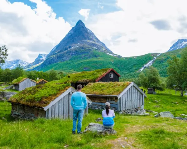 Para zwiedza ekuz w Norwegii, podziwiając tradycyjne chaty z zielonymi dachami i majestatyczne góry.