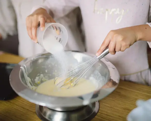 Préparation de la pâte à crêpes : on ajoute du sucre dans le bol avec un fouet. C'est la base de la recette des crêpes.