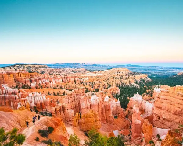 Zachód słońca nad Bryce National Park. Wąwóz pełen pomarańczowych hoodoos i zielonych drzew, z turystami na szlaku.