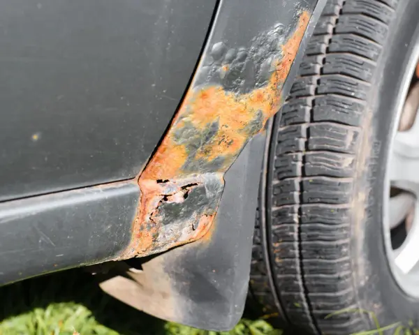 Rostfläckar och skador på bilens skärm nära däcket. En del av lacken har bubblat sig och metallen är synlig. Dags att ta bort repor på bilen och fixa rosten!