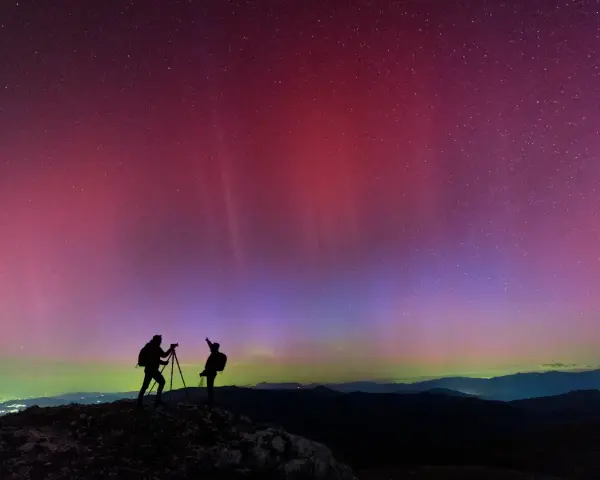 Due fotografi ammirano l'incredibile aurora boreale in Italia, con sfumature rosa e viola che danzano nel cielo stellato.