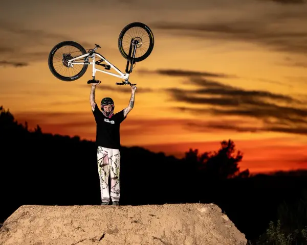Tomas Lemoine triumphantly raises his bike against a fiery sunset, a champion on the dirt jump.