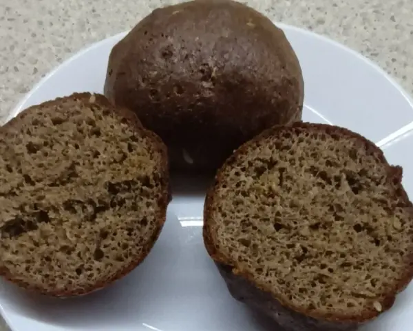 Na talerzu leżą keto bułki babka jajowata. Jedna jest cała, dwie pozostałe przekrojone na pół, ukazując puszyste wnętrze.