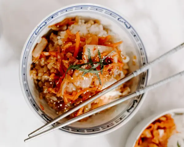 Miseczka ryżu z pikantnym kimchi i marchewką, idealne połączenie. Pałeczki czekają, by zacząć jeść.