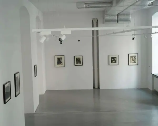Galeria sztuki z pracami Karola Hillera. Wnętrze z białymi ścianami, szarą podłogą i kilkoma czarno-białymi fotografiami na ścianach.