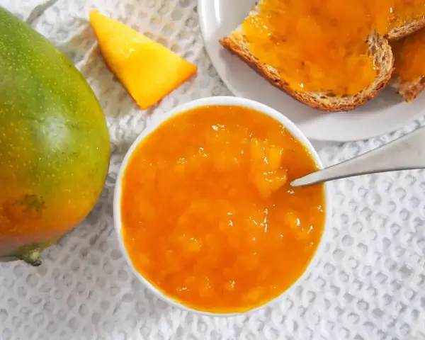 Słoik z dżemem z mango, obok świeży owoc i kromki chleba. Codzienne jedzenie mango to pyszny początek dnia.