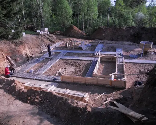 Budowa fundamentów: zbrojenie i szalunki czekają na chudy beton. W tle las i plac budowy.