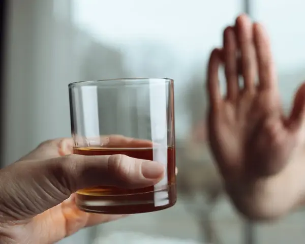 Dłoń odrzuca szklankę z alkoholem, symbolizując koniec z nałogiem i wyciek z wszywki.