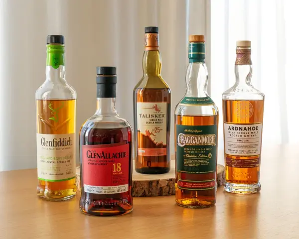 Fünf Flaschen gute Whiskey-Sorten: Glenfiddich, Glenallachie, Talisker, Cragganmore und Ardnahoe stehen auf einem Holztisch.