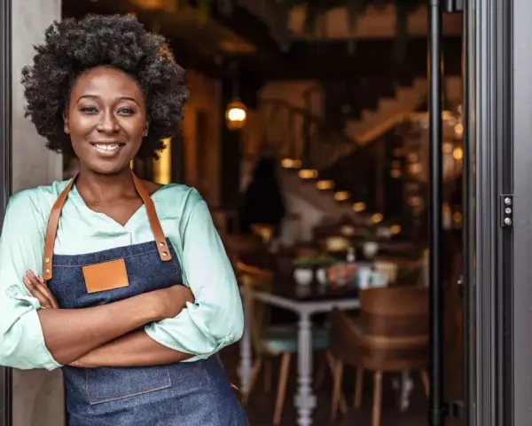Mujer sonriente con delantal, lista para abrir su restaurante. Su plan de negocio es sólido.