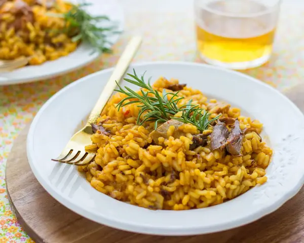 Delicioso arroz con setas y carne, servido en plato blanco con tenedor dorado y ramita de romero.