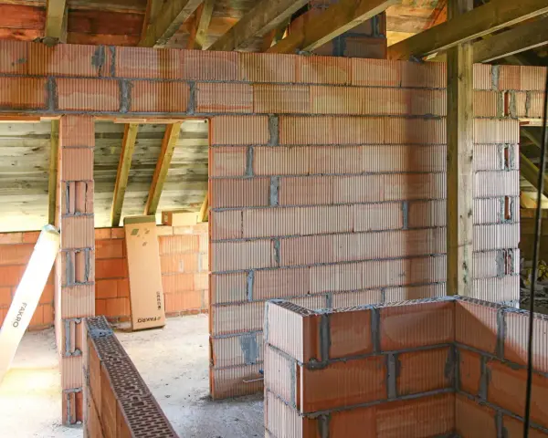 Budowa domu w trakcie. Widać ściany z pustaków ceramicznych, drewniane belki stropowe. Murowanie na piankę wady mogą pojawić się przy niedokładnym wykonaniu.