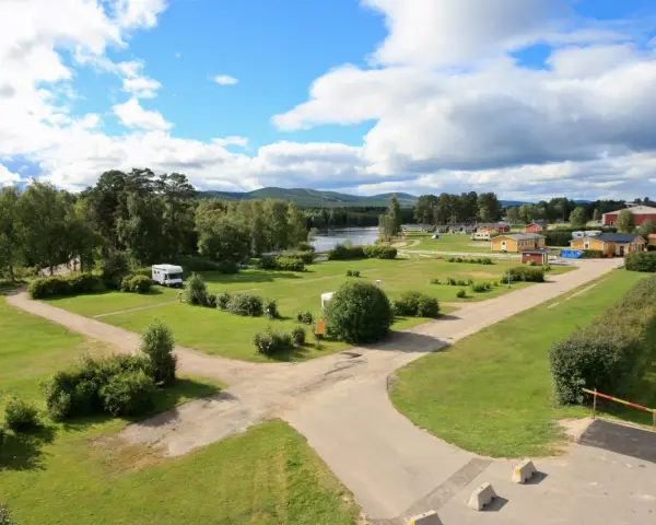 Vacker vy över svegs camping med husbilar, stugor och en sjö i bakgrunden under en molnig himmel.