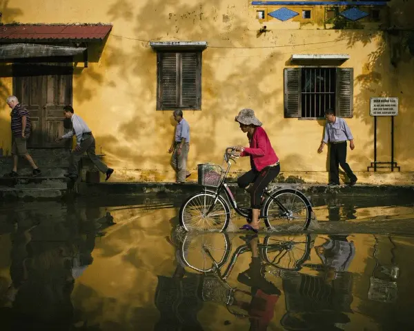 Une femme à vélo traverse une rue inondée, reflétant la vie quotidienne. Quel objectif pour photo de rue capture cette scène ?
