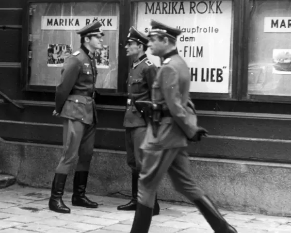 Trzej żołnierze w mundurach stoją przed kinem z plakatem Mariki Rökk. Stawka większa niż życie, teatr historii.