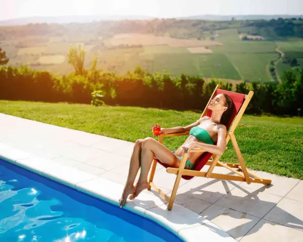 Donna rilassata su una sdraio, con drink, vicino a una piscina. Il sole splende, ideale per chi vuole sapere come abbronzarsi velocemente.
