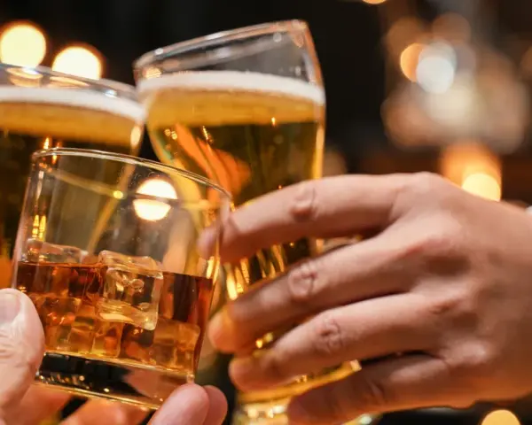 Trzy dłonie wznoszą toast: jedna z whisky na lodzie, dwie z piwem. Lepiej 2 drinki czy 2 piwa?