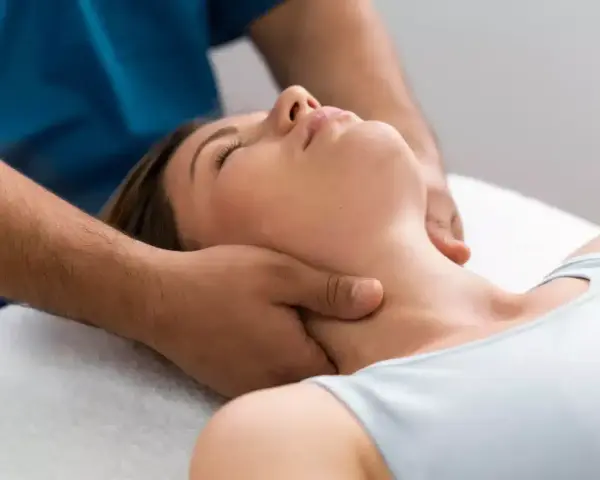 Fizjoterapeuta delikatnie masuje szyję kobiety, łagodząc napięcie. To jak ulga, gdy znika uczucie włosów w gardle.