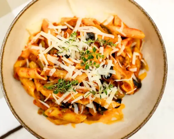 Penne z bogatym sosem anchois, czarnymi oliwkami i parmezanem, udekorowane świeżym tymiankiem.