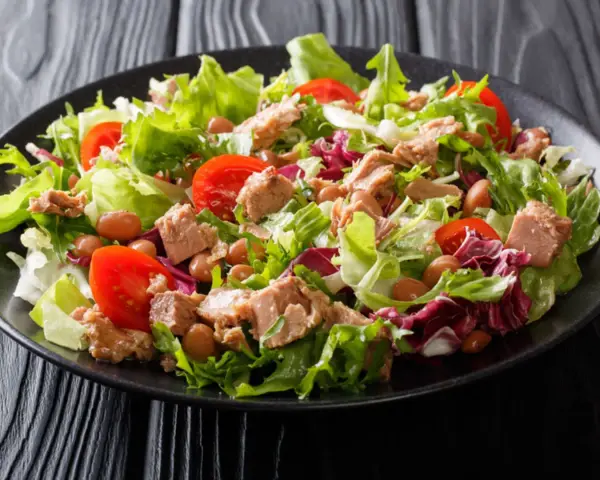 Ein frischer Thunfischsalat mit knackigem Salat, Tomaten und Bohnen auf einem schwarzen Teller.