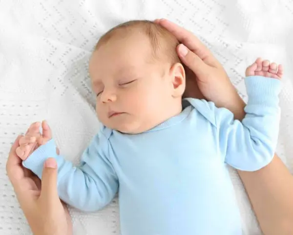 Un neonato dorme sereno sul petto della mamma, cullato dalle sue mani.