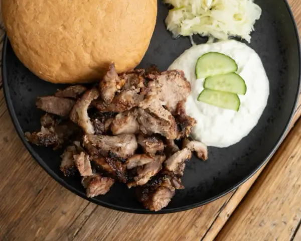 Ein Teller mit gegrilltem Fleisch, einem Brötchen, Tzatziki und Krautsalat. Perfekt für ein leckeres Gyros Rezept.