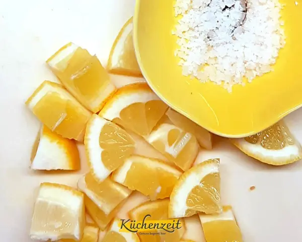 Frische Zitronenspalten und grobes Salz in einer gelben Schale – die perfekte Basis für viele Rezepte mit Zitrone.
