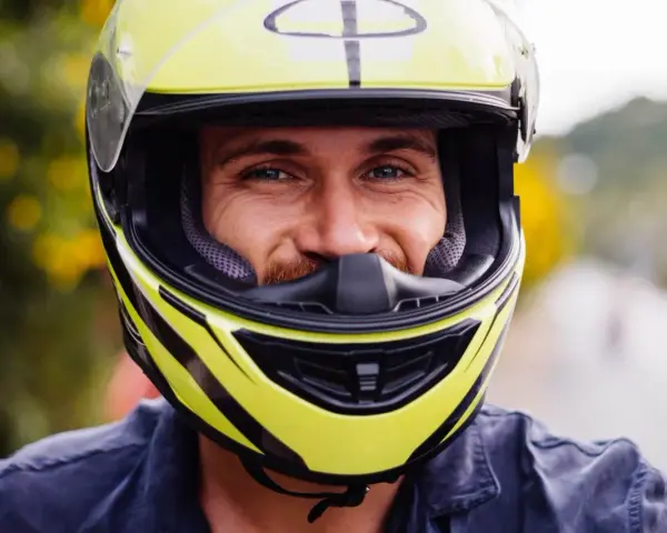 Uśmiechnięty mężczyzna w żółtym kasku motocyklowym z czarnymi elementami.