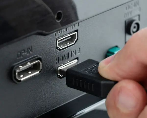 Hand steckt HDMI-Kabel ein, um den PC mit dem Fernseher zu verbinden. Anschlüsse für DisplayPort und HDMI sind sichtbar.