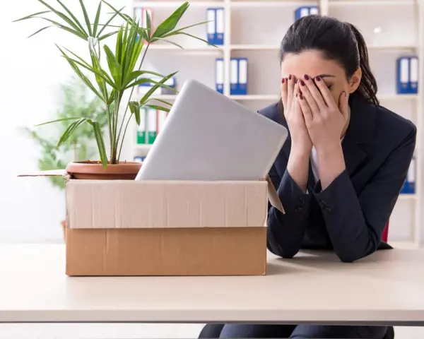 Verzweifelte Frau mit Karton und Laptop im Büro. Sie muss eine innerbetriebliche Versetzung ablehnen und ist sichtlich mitgenommen.