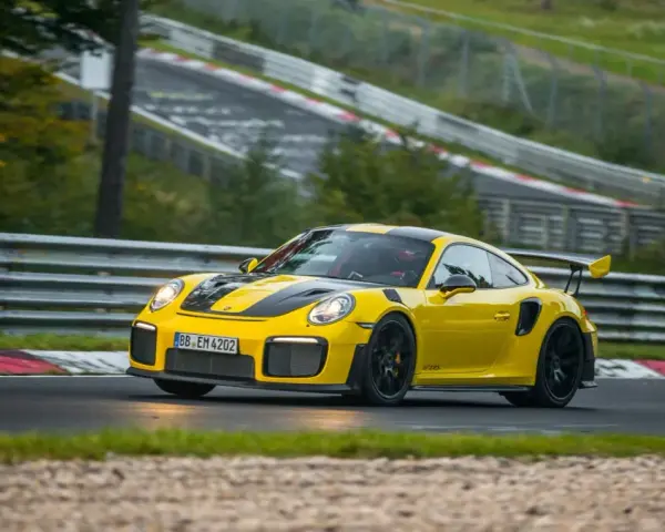Żółty Porsche 911 GT2 RS z czarnymi pasami pędzi po torze wyścigowym.