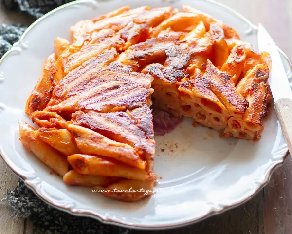 Una deliziosa frittata di pasta, dorata e croccante, servita su un piatto bianco con un coltello.