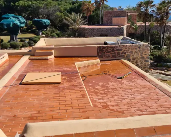 Proceso de impermeabilizar terraza con acabado de tejas rojas. El sol brilla sobre la superficie mojada, lista para proteger la casa.