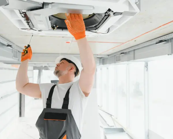 Técnico revisa aire acondicionado en techo, una señal para saber si le falta gas al aire acondicionado es que no enfría.
