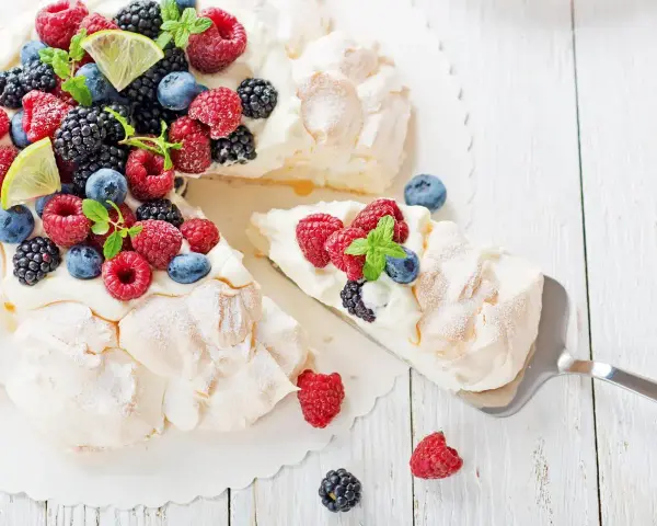 Beza pavlova która zawsze wychodzi, udekorowana świeżymi malinami, borówkami, jeżynami i plasterkami limonki.