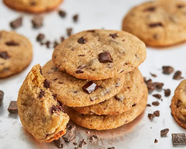 Ein Stapel saftiger american cookies mit Schokoladenstückchen, einer angeknabbert, umgeben von Schokoladenstückchen.