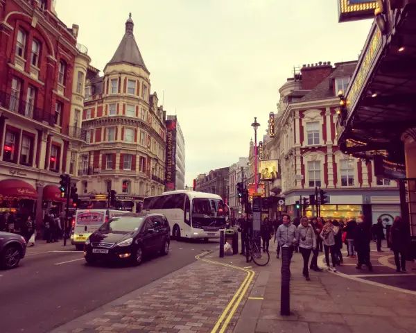 Tętniące życiem ulice Soho w Londynie, z charakterystyczną architekturą, autobusami i ludźmi spacerującymi po chodniku.