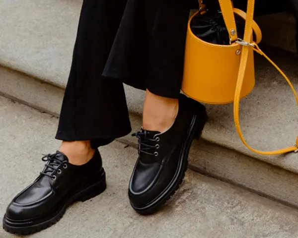 Come abbinare le stringate femminili: look audace con pantaloni neri e borsa gialla.