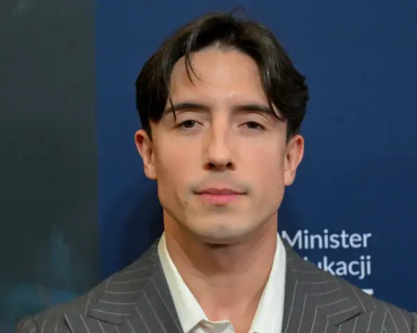 Dawid Kwiatkowski w szarym garniturze na tle niebieskiej ściany z napisami.