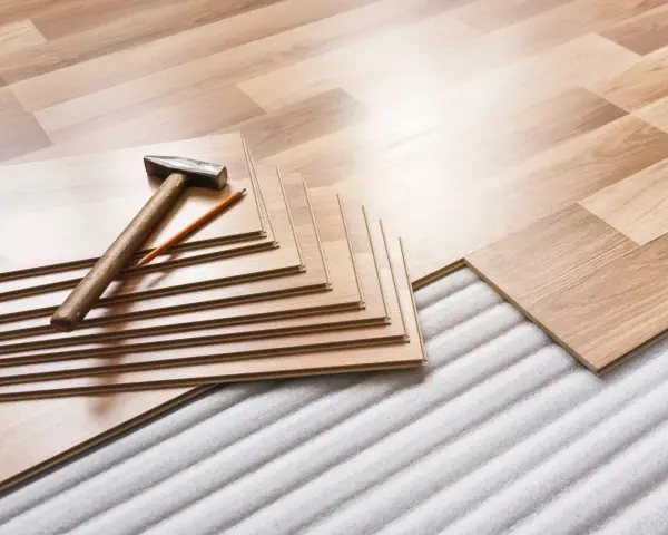 Tablas de suelo laminado apiladas con martillo y lápiz, listas para aislar suelo frío sobre una base acolchada.