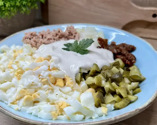 Pyszna sałatka z tuńczykiem, jajkiem, ogórkiem kiszonym i suszonymi pomidorami, polana majonezem.