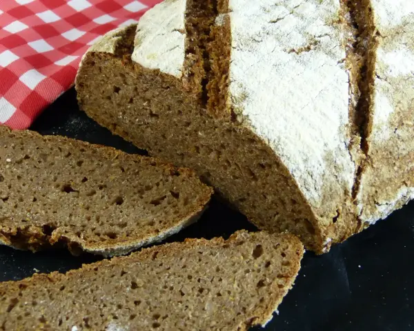 Ein rustikales tschechisches Brot, frisch aufgeschnitten, mit einer kräftigen Kruste und einer saftigen Krume. Daneben liegt eine rot-weiß karierte Serviette.