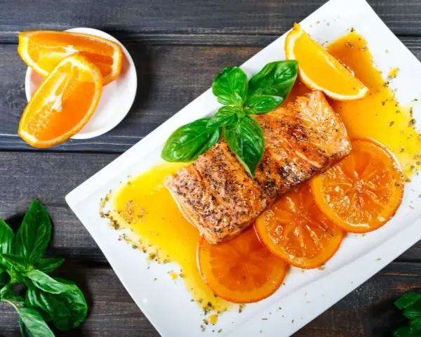 Delicioso salmón a la naranja, servido con rodajas de naranja y hojas de albahaca fresca.
