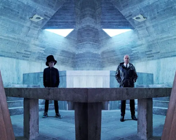 Pet Shop Boys in futuristischer Betonarchitektur. Neil Tennant mit Zylinder, Chris Lowe im glänzenden Mantel.