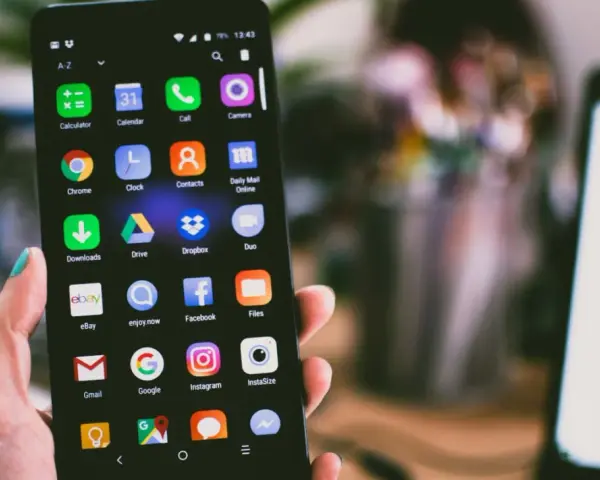 Dłoń trzyma smartfon z widocznym ekranem pełnym ikon aplikacji, w tym ikoną wiadomości SMS.