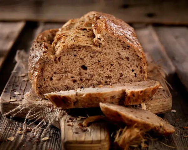 Frisch gebackenes Körnerbrot, angeschnitten auf einem Holzbrett. Perfekt, wann Brot aus der Form nehmen, um diese Kruste zu erhalten.