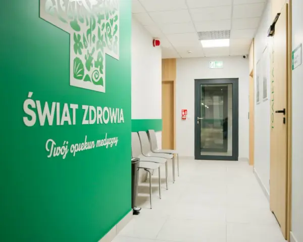 Zielona ściana z napisem "Świat Zdrowia" i logo, korytarz kliniki medycznej z drzwiami i krzesłami.