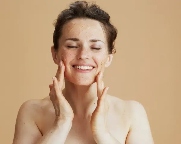 Kobieta z zamkniętymi oczami delikatnie masuje twarz peelingiem. Zastanawiasz się, ile razy w tygodniu robić peeling?